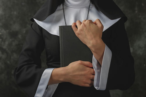 shutterstock_509116372.jpg A nun in traditional attire holding a book close to her chest