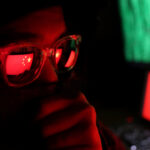 Illegal Chinese Police Station BUSTED in Manhattan… Person wearing glasses with a reflection of the Chinese flag, surrounded by computer screens