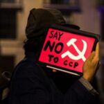 CHINA-FUNDED Billionaire Bankrolls “Anti-Billionaire” Movement… Person holding a protest sign that reads Say NO to CCP with a communist symbol