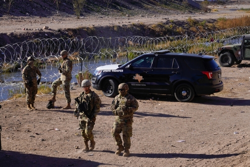 shutterstock_2241074351.jpg Military personnel and law enforcement officers near a border area with vehicles and barbed wire