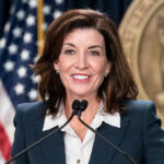Crowd Drowns Out Governor At Ryder Cup Woman speaking at podium with American flag behind.