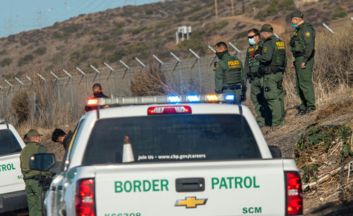 shutterstock1900868446-1jpg Border Patrol agents gather near trucks by a fence