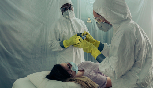 Two,People,Attending,To,A,Woman,With,A,Virus,Lying Healthcare workers in protective gear attending to a patient