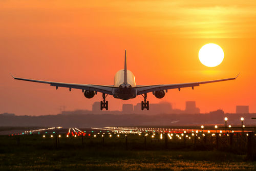 shutterstock_419990866 Airplane landing at sunset on illuminated runway.