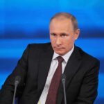 Mystery Whale Bets Against Putin A serious-looking political figure seated at a press conference with a blue background