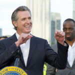 Lawmen Blast Newsom Over Funding Smiling man giving a speech at an outdoor event.