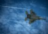 Jet fighter flying through a cloudy blue sky leaving vapor trails