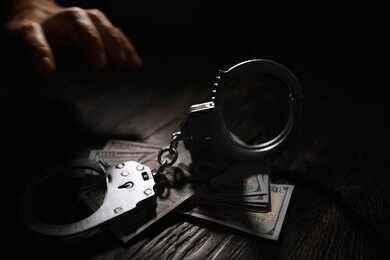 2719486809-1 Handcuffs on cash with a reaching hand in low light