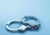 UK Extradition Hunt Targets Influencer Duo Metal handcuffs on a light blue surface