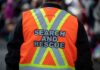 Search and rescue worker in an orange reflective vest seen from behind