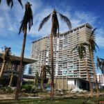 Damaged residential building surrounded by palm trees after a storm