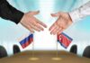 Nuclear Duo Tightens Grip — What’s Coming? Two hands reaching to shake over small Russian and North Korean flags