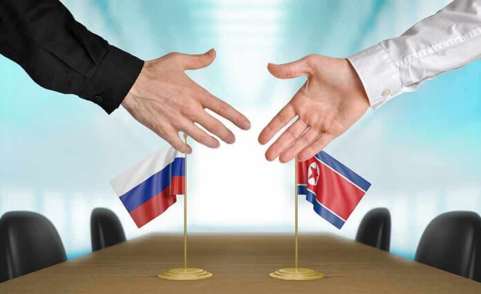 shutterstock_281935505 Two hands reaching to shake over small Russian and North Korean flags