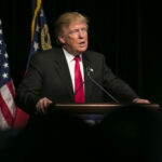 Trade Cut Threat Stuns Spain Donald Trump speaking at event with American flags.
