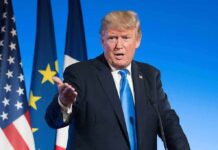 New Claims About Trump Scrutinized man in suit speaking at podium with flags behind
