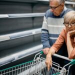 Worried elderly couple before empty supermarket shelves.