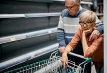 Worried elderly couple before empty supermarket shelves.