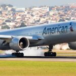 Airplane landing on runway with city in background.