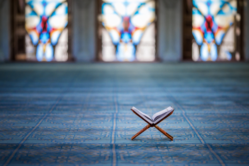 Quran on stand inside mosque with stained glass windows.