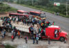 Crowded truck carrying people, buses on road nearby.