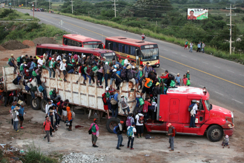 Crowded truck carrying people, buses on road nearby.