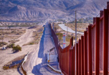 Border wall stretching through desert landscape with mountains.