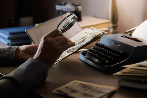 Person examining documents with magnifying glass near typewriter.