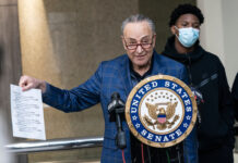 Chuck Schumer holds document at United States Senate podium.