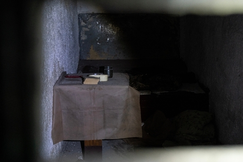 Dimly lit prison cell with small table and items.