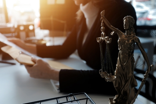 Person holding documents, Lady Justice statue in foreground.