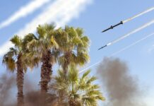 Missiles flying over palm trees with smoky sky.